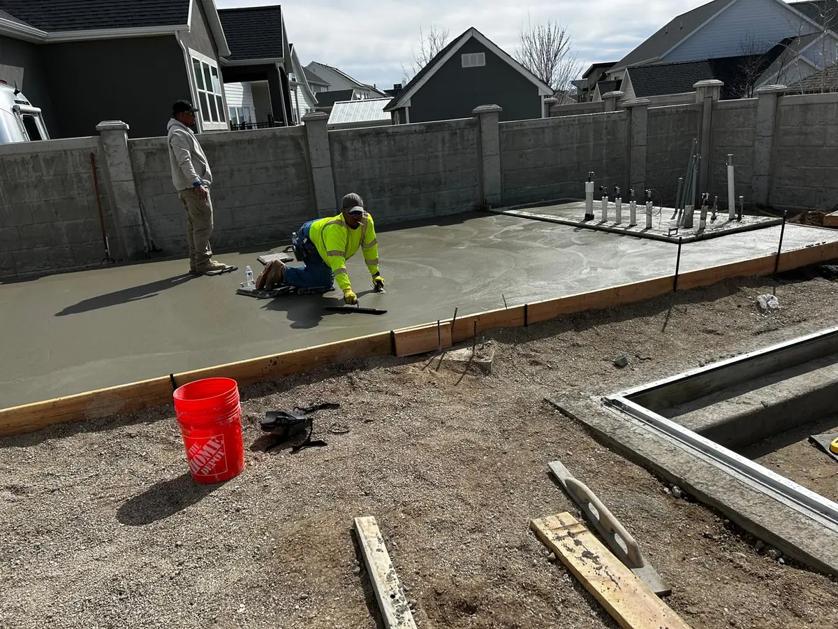 Worker finishing concrete flatwork by hand inside timber forms